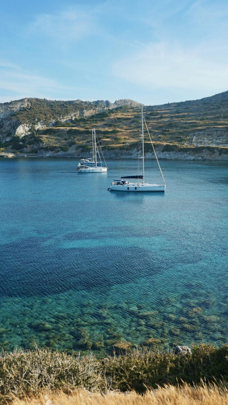 Tranquil Mediterranean bay view featuring anchored sailboats and clear turquoise waters.