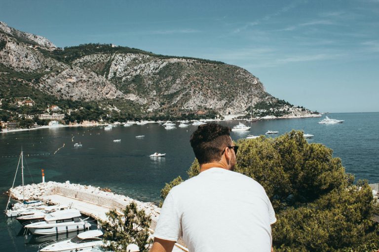 Traveler enjoying the picturesque harbor view at the French Riviera with sailboats and mountains.